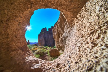 Kelso ve Duvardaki Delik 'in yakınındaki Mojave' deki kayalık bir kemerin içinden dramatik bir güneş doğuyor. Güneş ışığı, Kaliforniya 'nın özünü yansıtan desenli taş ve vahşi çöl manzarasını aydınlatır.