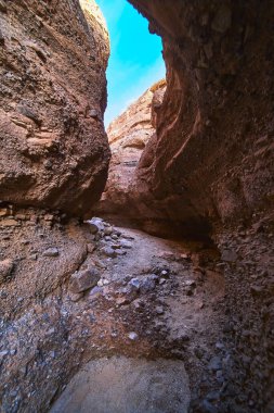 Arizona 'daki Ürkütücü Kanyon' dan geçen güneş ışığı filtreleri desenli slot kanyonu duvarlarını ve kayalık kumlu zemini ortaya çıkarıyor. Yukarıdaki canlı mavi gökyüzü kontrastı ekler ve hissi artırır