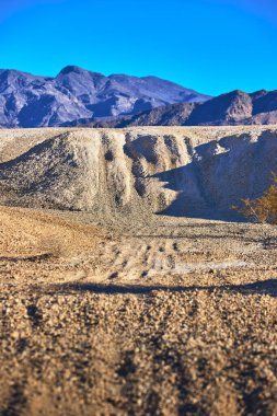 Sıcak altın saat güneşi Las Vegas Nevada yakınlarındaki Tule Springs Fosil Yatağı 'nda çakıl tepelerini ve engebeli tepeleri aydınlatıyor. Uzak dağ sıraları ve berrak gökyüzü macera ve yalnızlık hissi uyandırıyor..
