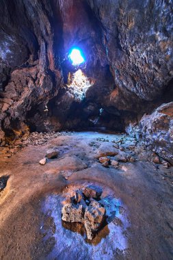 Mojave Çölü Kaliforniya 'daki Kelso Lava Tüneli' nin çatı penceresinden güneş ışığı akmaktadır. Rocky mağara duvarları ve dağınık taşlar Amerika Birleşik Devletleri 'nde dramatik bir doğal manzara yaratıyor..