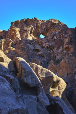 Güneş ışığı, Kelso California yakınlarındaki Mojave 'de engebeli kaya kemerini ve duvardaki delik oluşumunu vurguluyor. Parlak mavi gökyüzü, çarpıcı bir çöl manzarası yaratan desenli taşla çelişiyor..