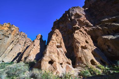Doğal delikli dramatik volkanik kaya oluşumları Kelso California yakınlarındaki Mojave arazisine hakim. Çöl bitkileri ve canlı mavi gökyüzü engebeli güzellikleri yansıtan bir sahne yaratıyor.