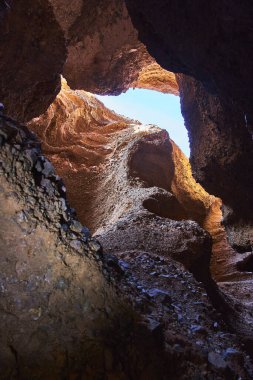 Arizona 'daki Ürkünç Kanyon' un dar açılışına güneş ışığı akar ve dramatik kaya duvarlarını ve dokularını vurgular. Yukarıya bakan manzara, taş toprak renkleri ve parlak gökyüzünün çarpıcı bir kontrastını yakalar.