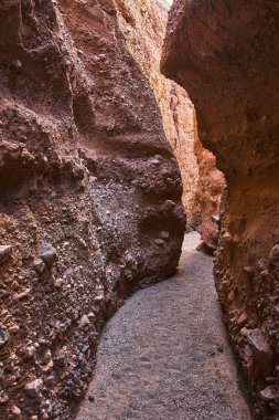 Arizona 'daki Ürkütücü Kanyon Kanyonu' ndan geçen dar geçit rüzgarları. Güneş ışığı desenli kaya duvarlarını ve kumlu zemini vurgular macera ve keşif hissi yaratır..