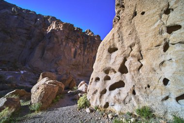 Güneş ışığı, Kelso California yakınlarındaki Mojave Çölü 'nün Duvardaki Delik bölgesinde desenli kumtaşı kayalıkları ve dağınık kayaları aydınlatır. Dramatik kaya oluşumları canlı bir mavi altında göze çarpar.