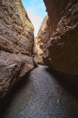 Arizona 'da Spooky Canyon' daki çakıllı bir yolun üzerinde yükselen kumtaşı duvarlar. Parlak mavi gökyüzü, Amerika 'da macera ve gizem hissi yaratan dar kanyondan bakıyor.