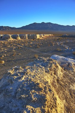 Sıcak altın saat ışığı, Nevada 'daki Tule Springs Fosil Yatağı' nda dokulu kaya oluşumlarını yıkar. Uzak dağlar ve geniş Las Vegas çölü Birleşik Devletler 'in zamansız güzelliğini çağrıştırıyor.