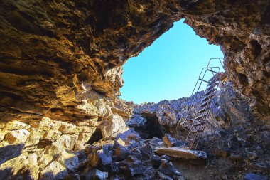 Güneş ışığı, Kelso California yakınlarındaki Mojave lav kanalının girişinde volkanik kayaları ve metal merdiveni aydınlatır. Sahne macera jeolojisini ve eşsiz çölü yakalıyor.