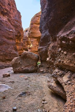 Güneş ışığı Arizona 'da Spooky Canyon' un dokulu kırmızı kaya duvarlarını aydınlatırken kumlu zeminde büyük bir kaya parçası duruyor. Dar kanyon dramatik ve maceralı bir hava yaratıyor.