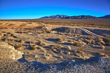 Altın saat ışığı, Las Vegas yakınlarındaki Tule Springs Fosil Yatağı 'nı engebeli çöl arazisi ve uzak dağ sıralarıyla aydınlatıyor..