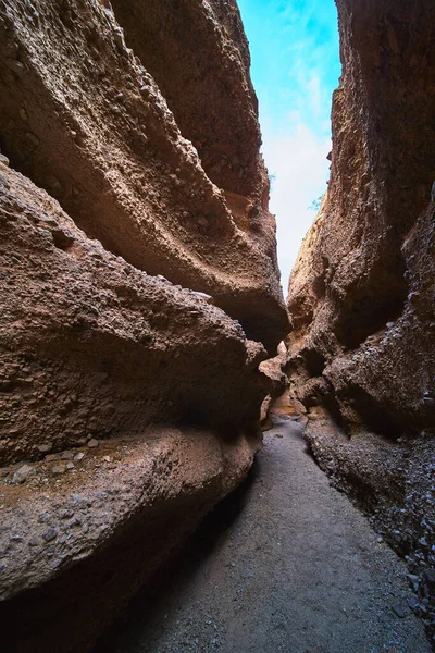 Yüksek kumdan duvarlar parlak mavi Arizona gökyüzünün altında kumlu bir kanyon yolunun üzerinde çarpıcı bir şekilde kıvrılıyor. Kaya yüzeyleri ve dar geçitler doğal bir merak hissi yaratıyor.