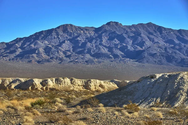 Altın saat güneş ışığı, Las Vegas yakınlarındaki Tule Springs Fosil Yatakları 'nı dramatik dağ arkaplanları ve engebeli çöl arazileriyle yıkıyor. Eşsiz jeolojik oluşumlar ve seyrek bitki örtüsü bunu doldurur.