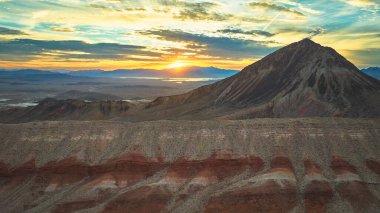 Las Vegas yakınlarındaki Lava Butte 'un hava manzarası. Güneşin doğuşuyla birlikte, dağı aydınlatan altın ışık ve dramatik bir gökyüzü altındaki canlı çöl arazisi..