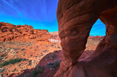 Las Vegas yakınlarındaki Ateş Kasesi 'nin geniş bir görüntüsünde belirgin bir kumtaşı kemeri dramatik kırmızı kaya oluşumları ve canlı mavi gökyüzü macera ve doğal güzellik hissi yaratıyor..
