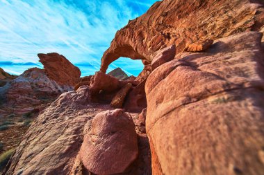 Las Vegas Nevada yakınlarındaki Ateş Kasesi 'nde sert kaya oluşumlarının üzerinde çarpıcı bir kırmızı kumtaşı kemeri yükseliyor. Canlı çöl renkleri ve açık gökyüzü dramatik ve maceracı bir Güneybatı Amerika Birleşik Devletleri yarattı.