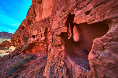 Rüzgarla oyulmuş oyukları olan canlı kırmızı kumtaşı kayalıkları Las Vegas Nevada yakınlarındaki Ateş Kasesi 'ne hakim. Parlak çöl arazisi ve berrak mavi gökyüzü dramatik ve maceracı bir Güneybatı manzarası yaratır..