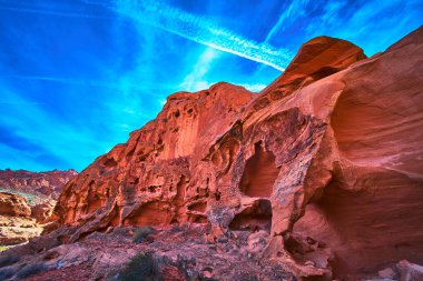 Çarpıcı kırmızı kumtaşı oluşumları Las Vegas Nevada yakınlarındaki Ateş Kasesi 'nde canlı mavi gökyüzüne karşı yükseliyor. Çöl bitki örtüsü ve dramatik erozyon desenleri bu ikonik Amerika Birleşik Devletleri 'ne derinlik katıyor.