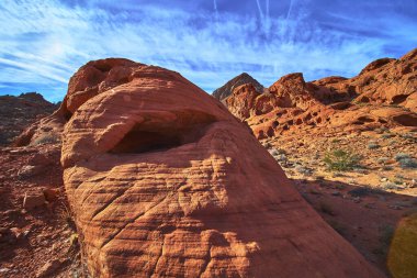 Parlak kırmızı kumtaşı oluşumları ve küçük bir mağara Las Vegas Nevada yakınlarındaki Ateş Kasesi 'nde güneş ışığını yakalıyor. Titrek gökyüzü ve engebeli arazi bu eşsiz Birleşik Devletler 'de bir macera hissi yaratıyor.