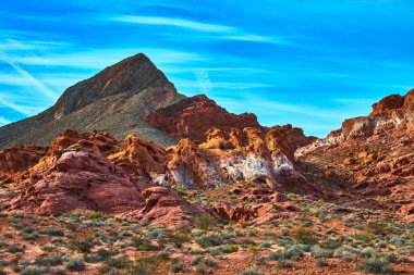 Canlı kırmızı kumtaşı oluşumları ve engebeli dağ zirveleri Las Vegas Nevada yakınlarındaki Ateş Kasesi 'ne hakim. Nadir bulunan çöl bitkileri ve parlak mavi gökyüzü dramatik bir güneybatı manzarası yaratır.
