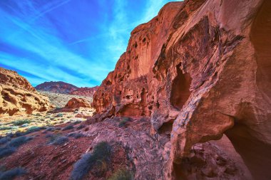 Etkileyici kırmızı kumtaşı kayalıkları parlak mavi gökyüzünün altında Las Vegas Nevada yakınlarındaki Ateş Kasesi 'ne hakim. Nadir çöl bitkileri ve engebeli dokular bu Birleşik Devletler 'in eşsiz güzelliğini vurguluyor.