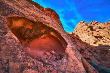 Las Vegas Nevada yakınlarındaki Ateş Kasesi 'nde mavi bir gökyüzünün altında dramatik bir mağara oyuğu olan canlı kırmızı kumtaşı oluşumları. Engebeli kayalıklar ve canlı renkler çarpıcı bir çöl yaratır.