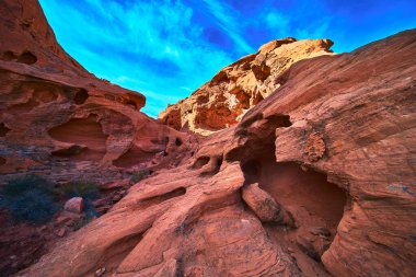 Güneşli kırmızı kumtaşı oluşumları ve doğal mağaralar Las Vegas Nevada yakınlarındaki Ateş Kasesi 'nde dramatik bir sahne oluşturuyor. Canlı mavi gökyüzü eşsiz kaya dokusunu ve dokunulmamış güzelliği vurgular.