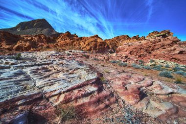 Vivid red sandstone rocks and rugged desert landscape stretch under a bright blue sky in the Bowl of Fire near Las Vegas Nevada. Unique rock textures and dramatic colors highlight the natural beauty