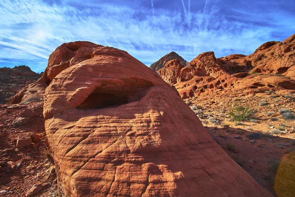 Parlak kırmızı kumtaşı oluşumları ve küçük bir mağara Las Vegas Nevada yakınlarındaki Ateş Kasesi 'nde güneş ışığını yakalıyor. Titrek gökyüzü ve engebeli arazi bu eşsiz Birleşik Devletler 'de bir macera hissi yaratıyor.