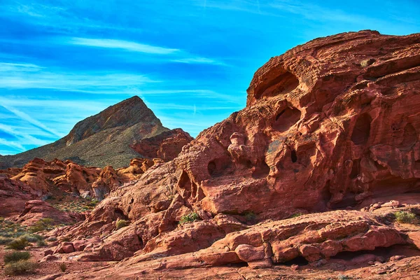 Canlı kırmızı kaya oluşumları arka planda engebeli bir dağ zirvesi ve ilham verici bir çöl sahnesi yaratan mavi gökyüzü ile Las Vegas Nevada yakınlarındaki Ateş Kasesi 'ne hakim..