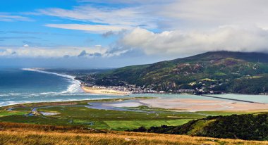 Morva 'nın yamaçlarından Barmouth ya da Abermaw adlı sahil kasabası dalgalı denizler, güneş ışığı ve yüksek fırtına bulutlarıyla Mawddach haliçlerinin panoramik manzarasını gösteriyor. Galler, İngiltere    