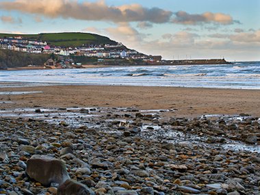 New Quay Limanı 'nın panoramik manzarası ve New Quay Körfezi' nden rıhtımı Galler 'in en iyi sahil yürüyüşlerinden biri. Resimde ayrıca filika istasyonu, balıkçı tekneleri ve su sporları için kullanılan kumlu koy da yer alıyor..         