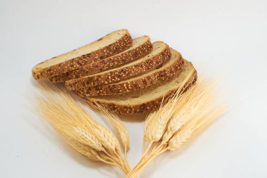 Beyaz zemin üzerinde dilimlenmiş tam buğday ekmeği, kesim için buğday yaprakları.