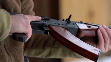 Bir adam elinde bir Kalaşnikof 47 tüfeği tutuyor, silahı kaldırıyor ve ateş etmek için bir pozisyon hazırlıyor. Yakın plan, tam otomatik, ses yok..