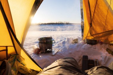 Cooking in the vestibule of a tent on a winter camping trip in Lapland.Sweden. clipart