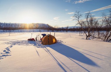 Kuzey Kutbu 'nun vahşi karlarında gün batımında çadır kuruyorlar. Laponya, İsveç.