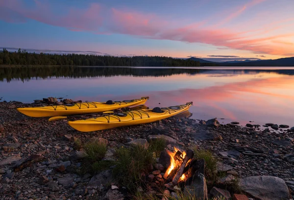 Alacakaranlıkta iki kanoyla gölün kıyısında kamp ateşi. Jamtland, İsveç.