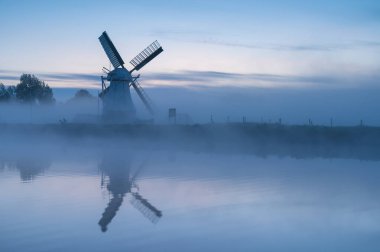 Windmill 'de Witte Molen' reflected in the canal during a foggy dawn in Holland.