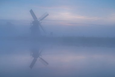 Windmill 'de Witte Molen' reflected in the canal during a foggy dawn in Holland.