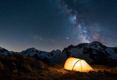 Illuminated red tent high in the mountains under the night sky with the milkyway.