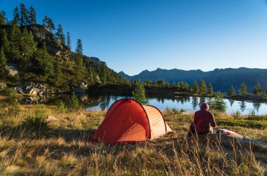 A woman at her red tent in the mountains on a summers mornig.