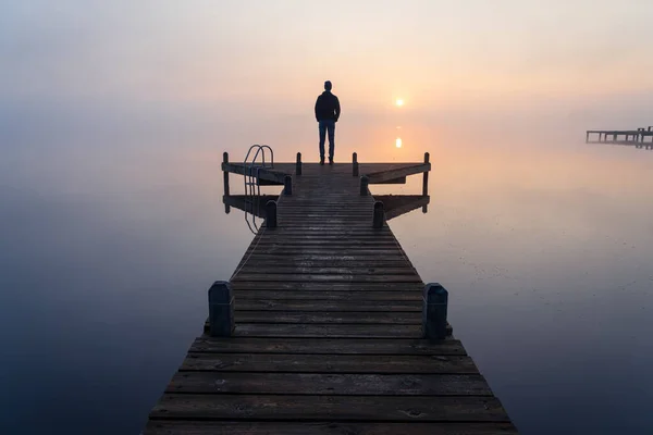 Sisli, sakin bir sabahta güneşin doğuşunu izleyen bir adamın silueti..