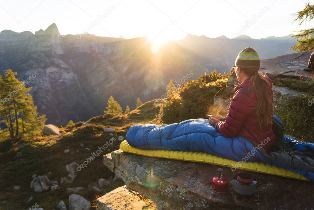 A woman cooking breakfast from her bivouac on a beautiful morning in the mountains.