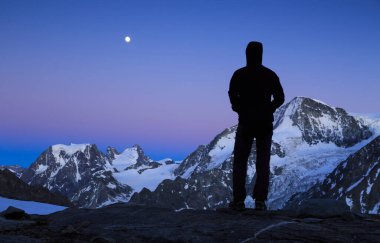 Dağcı, Wallis, Switserland 'daki dağların üzerinden yükselen aya bakıyor..