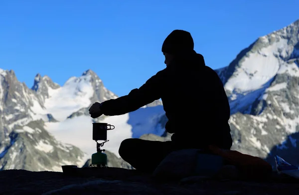 Hiker cooking on his bivouac in the Swiss mountains during dusk.