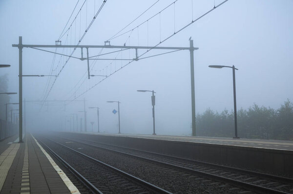 Woman alone at a trainstation, waiting for the trein on a foggy day in autumn.