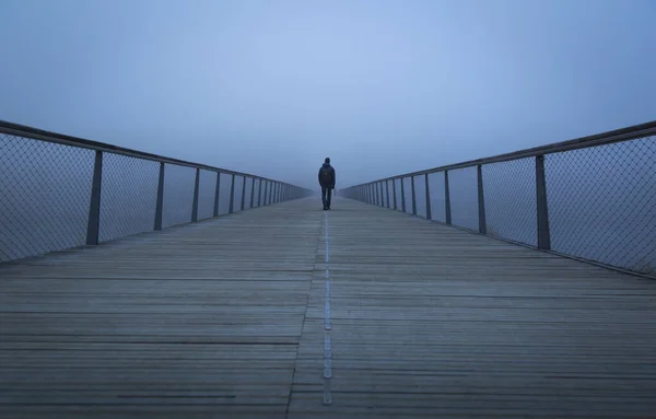Fransa 'nın Lyon şehrinin sabah sisine doğru modern bir yaya köprüsünde yürüyen bir adam. Sığ Savunma Bakanlığı..