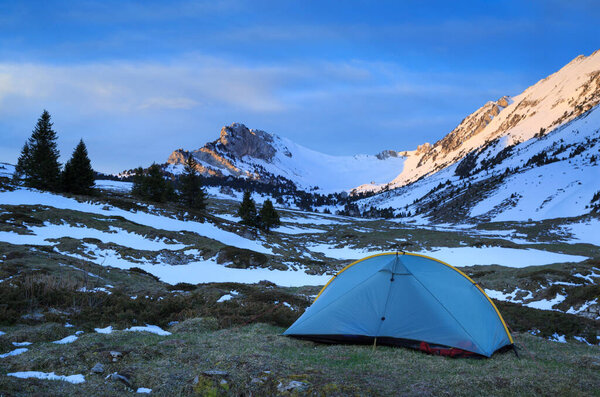 A tent in the mountains during a spring sunrise. 