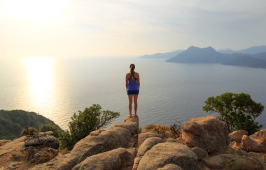Genç bir kadın ünlü Şato Kalesi yakınlarındaki kayalıklardan Porto Golf 'üne bakıyor. Korsika, Fransa.