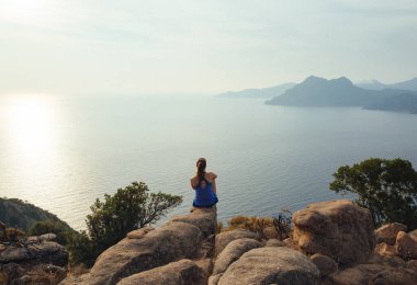 Kayalıklarda oturan ve Fransa, Korsika, Porto Golf 'üne bakan bir kadın. Eski film efekti.