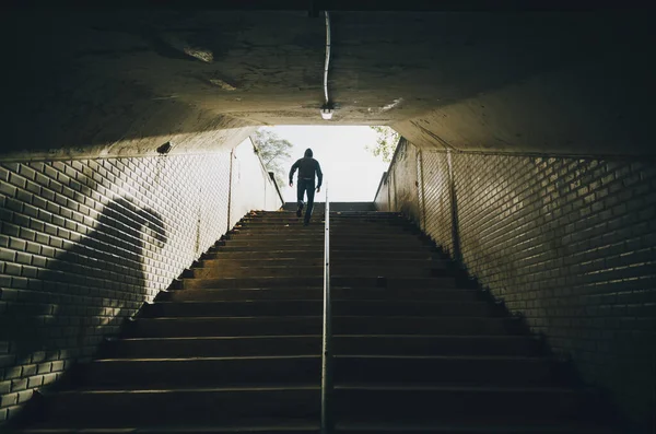 Şehirdeki eski bir tünelin merdivenlerinde koşan bir adam. Suç kavramı.
